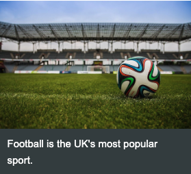 Crowd cheering at a British football stadium with players on the pitch